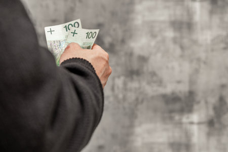 A man in a blue shirt and sweater holds money in his hand, counting the money.の写真素材