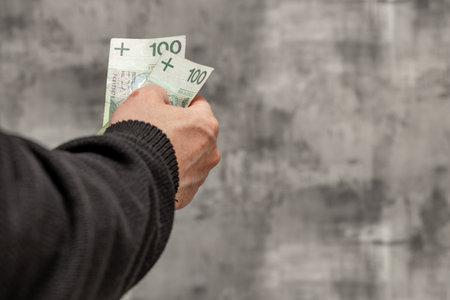 A man in a blue shirt and sweater holds money in his hand, counting the money before spending it.の写真素材