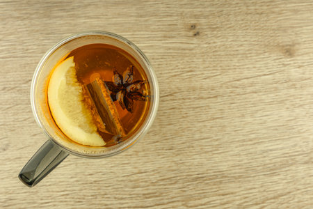 A clear double-walled glass filled with hot tea with oriental spices, cinnamon sticks, hibiscus, cloves, orange, star anise, a warming drink in a glass on a wooden tableの写真素材