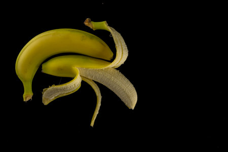 Two bananas arranged on a table, a peeled banana, an unpeeled banana, on a black backgroundの写真素材