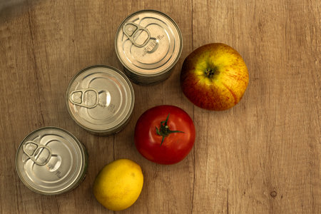 Three cans on a wooden table with tomatoes, lemon, and apples, healthy canned foodの写真素材