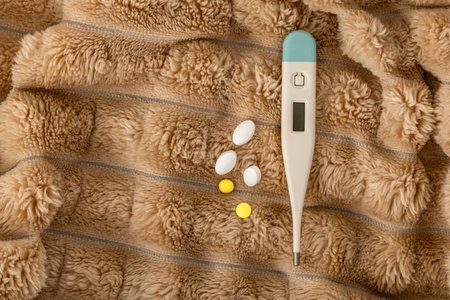 A thermometer showing a high temperature of a sick patient, home remedies for colds, an electronic thermometer and pills on a blanket in bedの写真素材