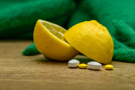 A lemon cut in half, vitamins, painkillers placed on a wooden counter, an electronic thermometer to measure fever, and tissuesの写真素材