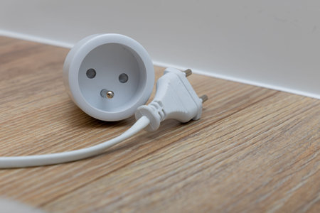 A plug with a cable placed on a wooden floor, a smart electrical outlet controlled by a phone