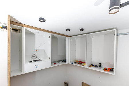White kitchen cabinets hung on the wall, assembly of custom-made kitchen furniture, assembling furniture from prefabricated components, fitting kitchen furniture, tools of the furniture assembly teamの写真素材