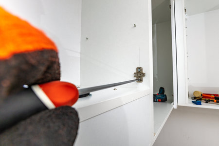 A carpenter wearing an orange protective glove assembles kitchen cabinets, leveling wall-hung cabinets, assembling kitchen furniture, a man assembling kitchen furniture wearing a protective gloveの写真素材