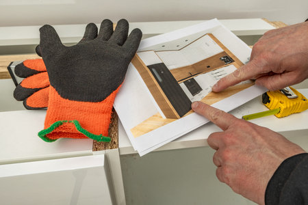 A carpenter makes corrections to a kitchen furniture design, a man in protective gloves clenches his...
