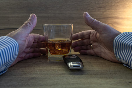 A driver dressed in an elegant shirt picks up a glass of whiskey with ice from a wooden counter, car...