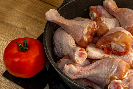 Chicken legs fried in a pan in oil, tomato and chicken pieces on an electric stove in a pan, raw chickenの写真素材