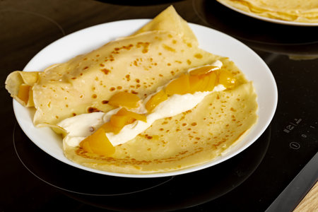 Fried golden yellow pancake batter on a white plate, spreading white cream cheese on pancakes, stuffing pancakes with peaches, realistic photoの写真素材