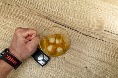 A man's clenched fists on a glass of vodka with ice cubes on a wooden kitchen counterの写真素材