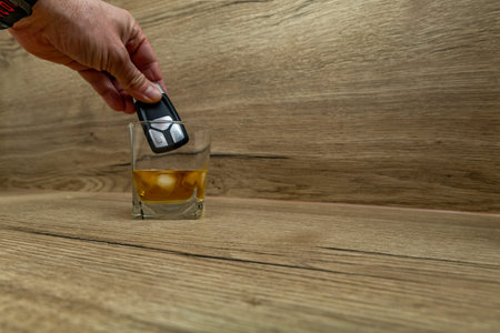 Person throwing car keys into whiskey with ice cubes
