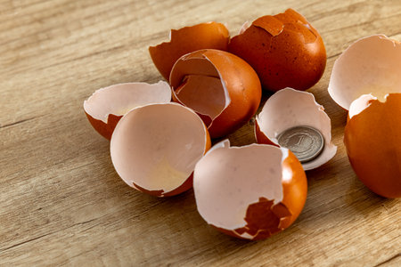 Chicken eggshells placed on a wooden counter in the kitchen, coins and banknotes placed inside the...