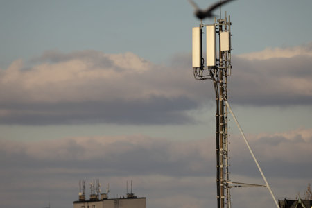 A tall mast with a mobile phone antenna against a blue sky, data transmission, an electromagnetic...