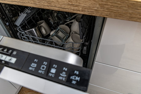 Loading dirty plates and cutlery into the dishwasher, preparing dishes for washing in the dishwasher, modern white kitchen furniture with a built-in dishwasher, glossy white kitchen cabinet frontsの写真素材