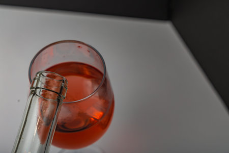 A glass of wine placed on a white countertop, the neck of a wine bottle from which wine is poured into the glass,の写真素材