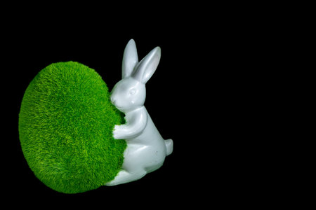 Figurines of little green bunnies holding an egg, Easter decorations, on a black background, a symbol of new lifeの写真素材