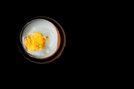 View of a boiled, peeled egg placed in a porcelain cup, a soft-boiled egg, a hard-boiled egg, on a black backgroundの写真素材
