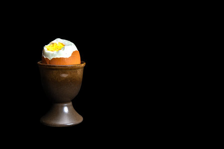 A boiled egg placed in a porcelain cup, a soft-boiled egg, a hard-boiled egg, on a black background