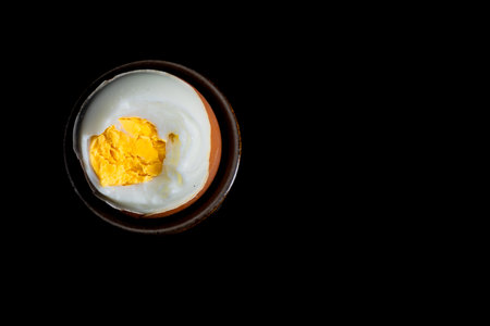 View of a boiled, peeled egg placed in a porcelain cup, a soft-boiled egg, a hard-boiled egg, on a black backgroundの写真素材