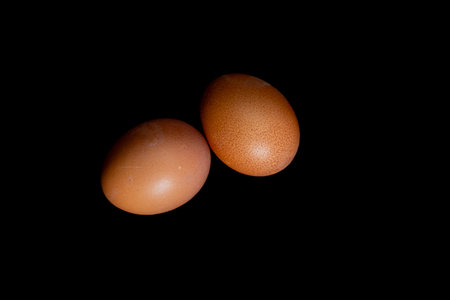 Two boiled eggs in orange shells on a black background, hard-boiled eggs, soft-boiled eggs