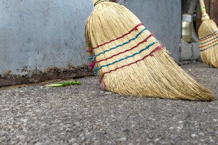 A broom leaning against a wall, ready for sweeping leaves, dust, and litter from an outdoor area. The simple composition represents cleanliness, housekeeping, maintenance, sanitation, and everyday cleaning tasks. Ideal for concepts related to home care, property maintenance, janitorial work, organization, and outdoor hygiene.