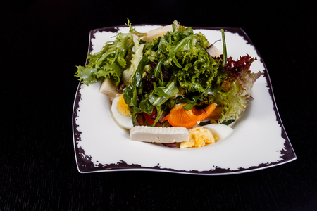 A colorful, tasty and healthy vegetable salat with red tomatoes, green cucumbers and pepper slices, white and yellow cheese, eggs and pesto sauceの写真素材