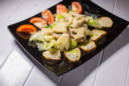Caesar salad with bacon and quail eggs Black plate on a white wooden backgroundの写真素材