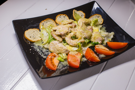 Caesar salad with bacon and quail eggs Black plate on a white wooden backgroundの写真素材