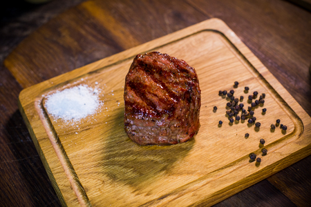 Beef steak on wood board with fork and knife, herbs spices and salt on a wood backgroundの写真素材