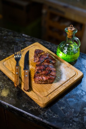 Juicy medium Beef Rib Eye steak on wooden board with fork and knife herbs spices and salt on a wood backgroundの写真素材