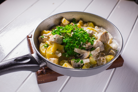 Fried potatoes with chicken, mushroom soup and onion in a boiler on a white wooden background.の写真素材