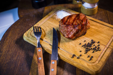 Beef steak on wood board with fork and knife, herbs spices and salt on a wood backgroundの写真素材