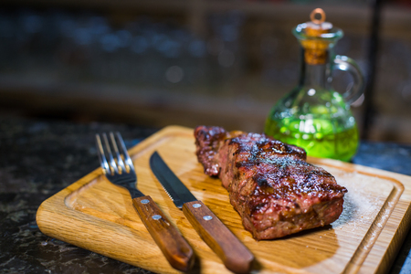 Juicy medium Beef Rib Eye steak on wooden board with fork and knife herbs spices and salt on a wood backgroundの写真素材