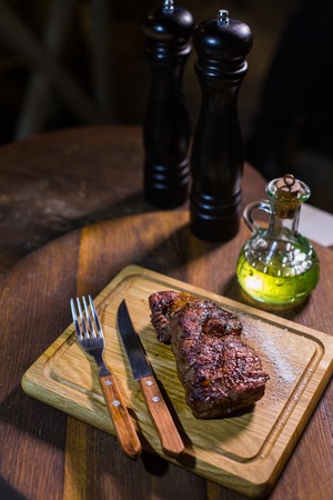 Juicy medium Beef Rib Eye steak on wooden board with fork and knife herbs spices and salt on a wood backgroundの写真素材