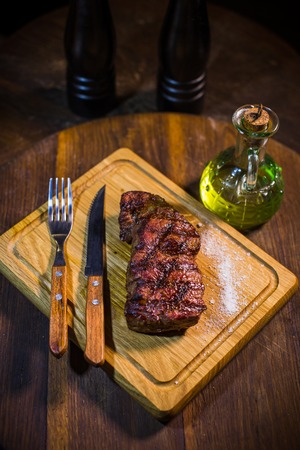 Juicy medium Beef Rib Eye steak on wooden board with fork and knife herbs spices and salt on a wood backgroundの写真素材