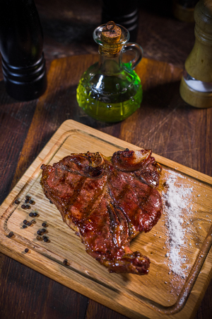 Grilled pork rib chop steak in a clay plate with oil, mustard, salt and rosemary is an old wooden background.の写真素材