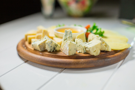 Different cheese on the table with honey and vegetablesの写真素材