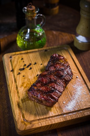 Grilled pork rib chop steak in a clay plate with oil, mustard, salt and rosemary is an old wooden background.の写真素材