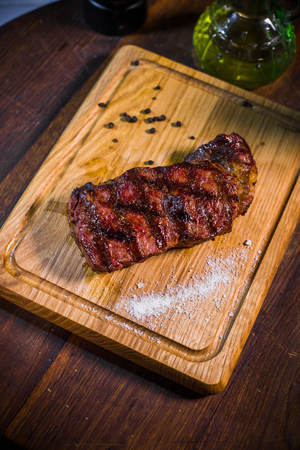 Grilled pork rib chop steak in a clay plate with oil, mustard, salt and rosemary is an old wooden background.の写真素材