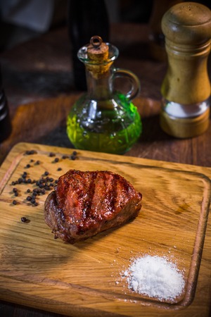 Grilled pork rib chop steak in a clay plate with oil, mustard, salt and rosemary is an old wooden background.の写真素材