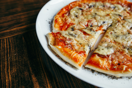Hot pizza slice with melting cheese on a rustic wooden table.の写真素材