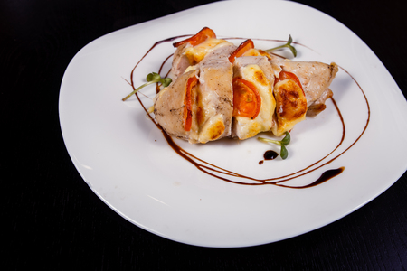 Spicy chicken fillet baked with bacon, tomatoes and cheddar cheese presented on a white plateの写真素材