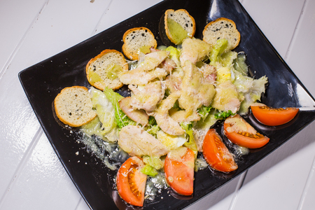 Caesar salad with bacon and quail eggs Black plate on a white wooden backgroundの写真素材