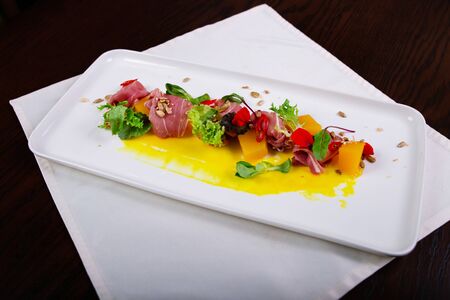 Pumpkin and gravy salad with Spanish jamon, pepper, herbs on a white plate decorated with seedsの写真素材