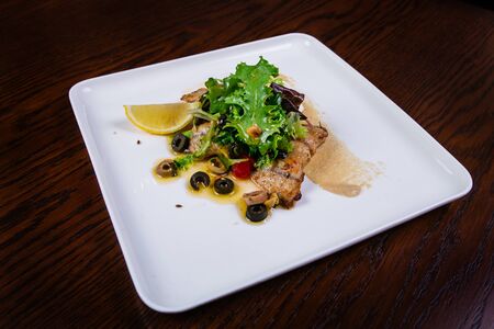 Grilled fish steak served with sauce and lemon, olives on dish. Close upの写真素材