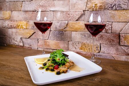 Grilled fish steak served with sauce and lemon, olives on dish. Close upの写真素材