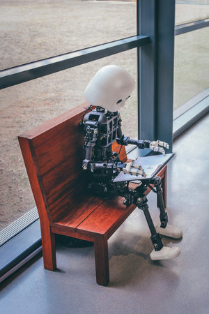 Robot sitting on a wooden chair in the office. Artificial intelligence concept.の写真素材