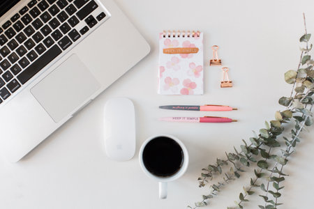 Flat lay workspace with laptop, coffee cup, eucalyptus branch and notebook on white background