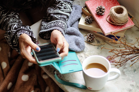 A young woman is sitting at home on the bed, drinking coffee and using a smartphone.の写真素材